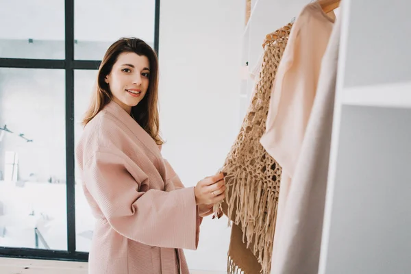 Leuke jonge vrouw staan in de voorkant van hanger rack en proberen om outfit te kiezen. — Stockfoto