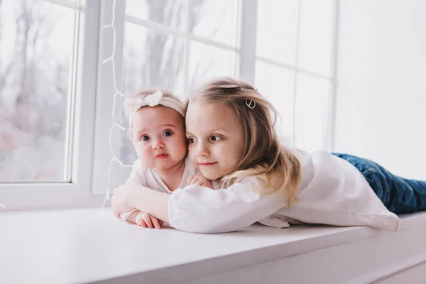 Deux sœurs mignonnes assis près de la fenêtre près de l'autre et jouer . — Photo