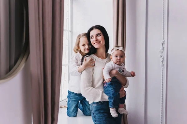 Portrét matka s dvěma dcerami v bílé místnosti u okna. — Stock fotografie