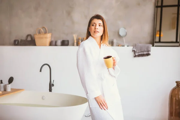 Hermosa mujer relajante en albornoz blanco cerca del baño — Foto de Stock