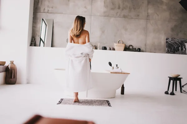 Hermosa mujer relajante en albornoz blanco cerca del baño — Foto de Stock