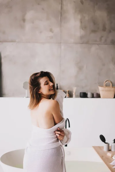 Mulher bonita relaxante em roupão de banho branco perto do banho — Fotografia de Stock