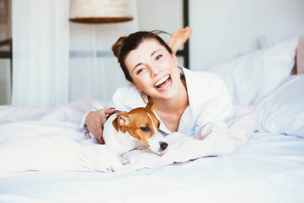 Kobieta i pies bawią się na łóżku. — Zdjęcie stockowe