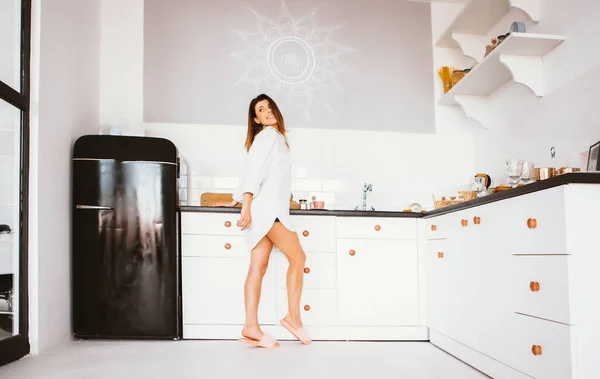 Muchacha joven en camisa blanca de pie en la cocina de la casa . — Foto de Stock