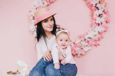 Anne ve kız oynuyor, öpüşüyor ve pembe arka planda çiçeklerle sarılıyorlar.. 