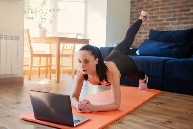 Egzersiz yapan, dizüstü bilgisayarda video izleyen, oturma odasında eğitim gören bir kadın. Vücut bakımı kavramı. 