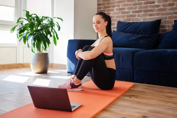 Woman training at home, doing exercises and watching videos on laptop, training in living room. Body care concept.