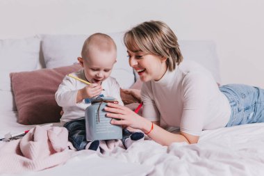 Genç anne ve 1 yaşındaki küçük oğlu yatakta kalemlerle oynuyorlar.