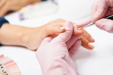 Manikür yaratma süreci. Tırnak törpüsü takan bir güzellik uzmanının manikür yaptırdığı bir kadının yakın plan fotoğrafı. Kadın manikür yaptırıyor. Güzellik uzmanı dosyasının bir müşteriye çivileri.