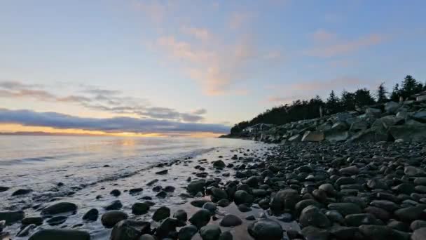 遠くの家と海岸にゆっくり波打つ波と美しい岩の海岸線 — ストック動画