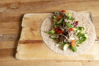 Sağlıklı bir jambon ve salatanın ahşap kesim tahtasına sarılı olduğu yakın plan görüntüsü. 