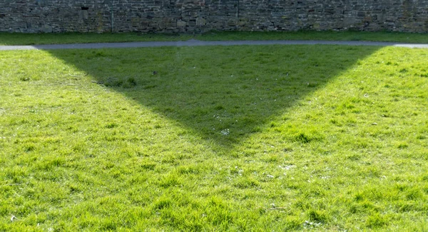 A close up view of the shadow of the church building on the grass in the open park next door to it