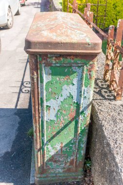 Boyanın soyulduğu binanın önündeki kaldırımda paslanmış eski bir elektrik kutusunun yakın görüntüsü.. 