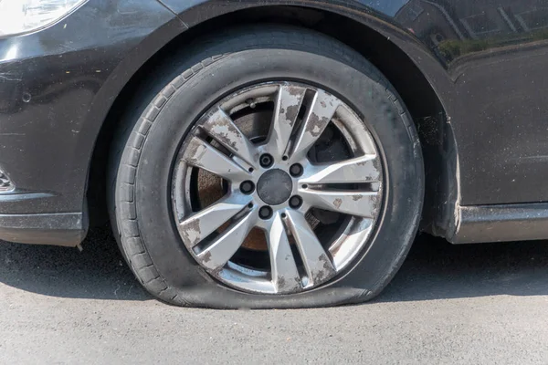 Yakın çekim. Yan sokağa park edilmiş lastiği patlamış bir araba. 