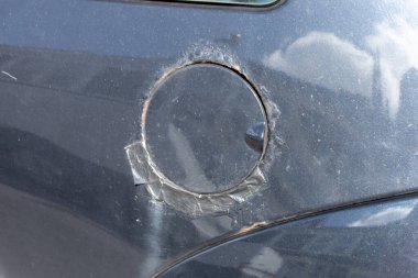 Siyah bantla paslanmış ve onarılmış siyah bir arabanın benzin kapağının yakın görüntüsü.