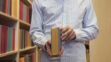 Kütüphanede kitaplığın önünde bir adam bir kitap seçer.