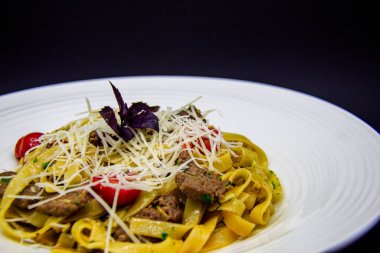 Siyah arka planda biftek ve kiraz domatesli makarna.