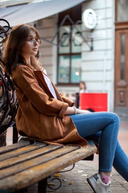 Sokakta gezen şık bir kız. Bej renkli yağmurluk, omzunda torba. Modern bir kadının resmi.