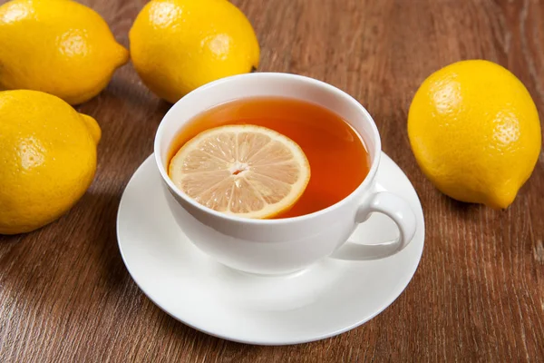 Натюрморт свежих лимонов на деревянном столе с чашкой чая — стоковое фото