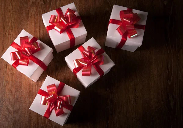 Beyaz şenlikli hediye kutuları ile ahşap bir masa üzerinde kırmızı yay — Stok fotoğraf
