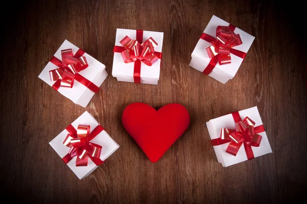 Beyaz şenlikli hediye kutuları ile ile ahşap bir masada kırmızı yay — Stok fotoğraf