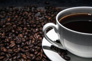 Bir fincan sıcak kahve ve kavrulmuş kahve çekirdekleri ahşap bir masada yakın planda.