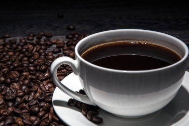 Bir fincan sıcak kahve ve kavrulmuş kahve çekirdekleri ahşap bir masada yakın planda.