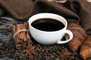 Bir fincan sıcak kahve ve kavrulmuş kahve çekirdekleri ve yakın plan kruvasanlar.