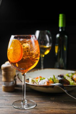 Parlak Aperol Spritz kokteyli, ahşap masada portakal ve buz. Biraz tabak ve arka plandaki şişe..