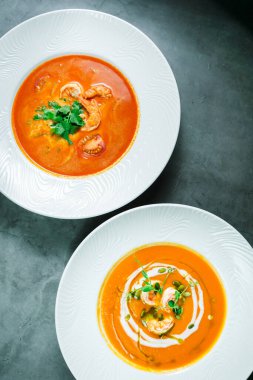 Taş bir tezgahın üstünde yeni pişmiş birkaç çorba. Tom Yum ve üstünde karides ve yeşillik olan bir balkabağı çorbası..