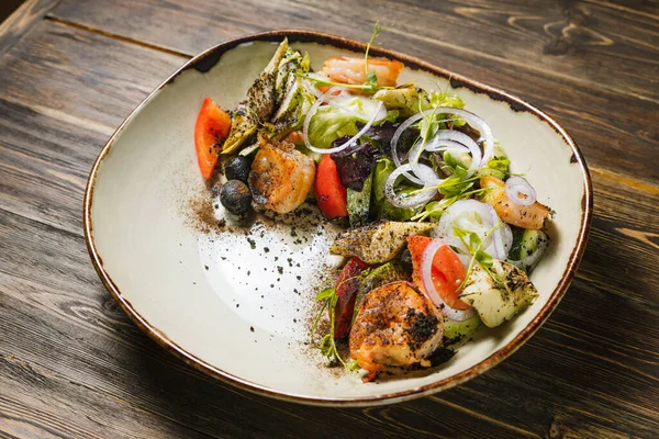 Karidesli, taze sebzeli, siyah zeytinli ve ahşap masadaki soslu taze salata..
