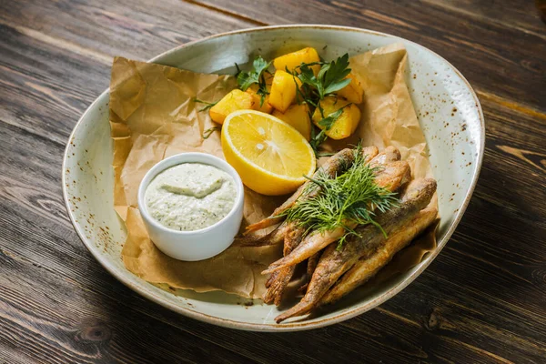Ahşap bir masadaki kağıt üzerinde fırında patates, limon ve sarımsak sosuyla nefis bir capelin..