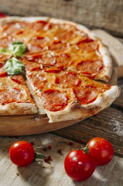 Lezzetli ev yapımı peynirli pizza, taze sebzeler ve ahşap masada pepperoni..