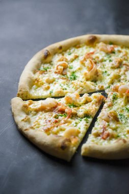 Taş tezgahın üstünde karides ve yeşillik olan lezzetli peynirli pizza..