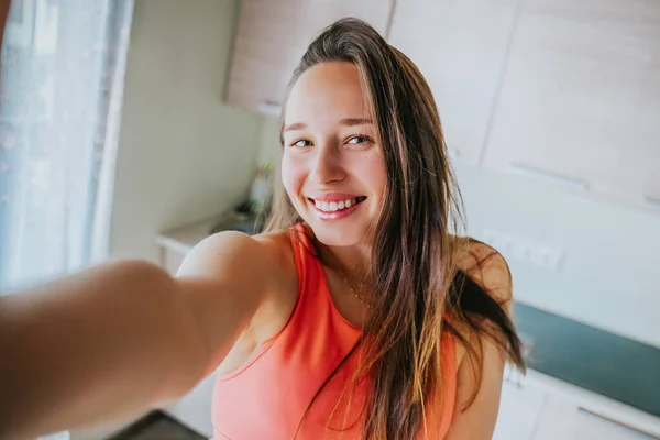 Genç ve neşeli bir kadın mutfakta selfie çekiyor.