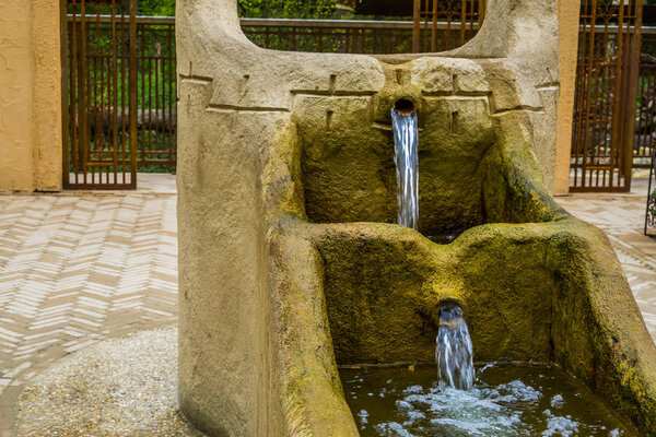 old vintage water fountain with streaming water, historical village architecture
