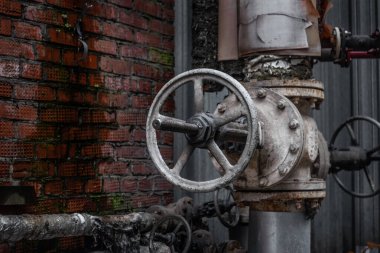 Eski su vanası. Tuğla bir duvarın arka planında eski bir su vanası. Su borusunda büyük ve paslı bir vana. Tuğla bir duvarın arka planında yakın plan.