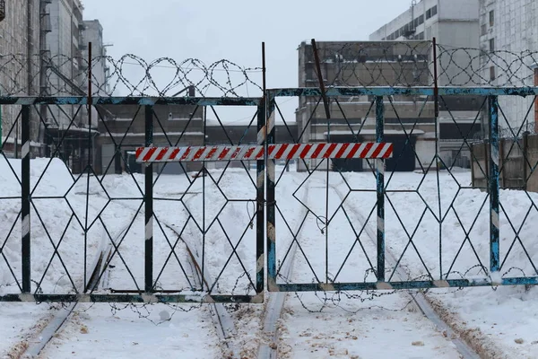 Closed factory gate with barbed wire. Winter, daylight.