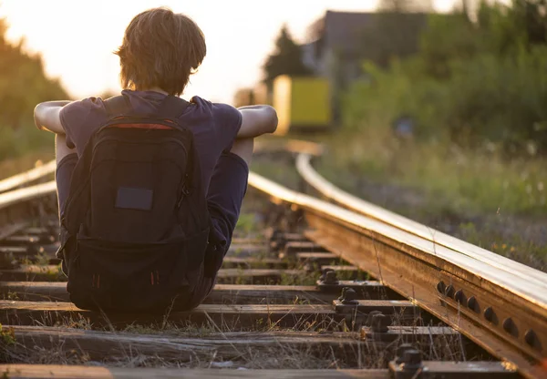 Yalnız bir çocuk tren raylarında oturur.