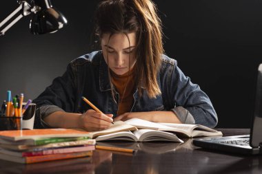 Kız masada oturuyor ve ders çalışıyor.