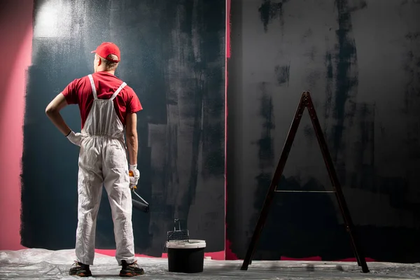 Man painting a wall. Painter in red overall painting wall in black color