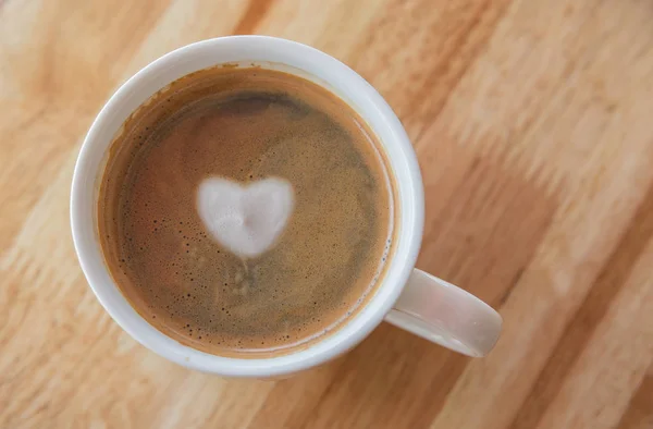 Corazón en taza de café con en una taza blanca sobre fondo de madera . — Foto de Stock