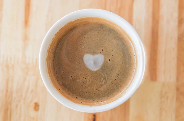 Καρδιά σε κούπα καφέ με σε ένα λευκό φλιτζάνι σε φόντο ξύλινη. — Φωτογραφία Αρχείου