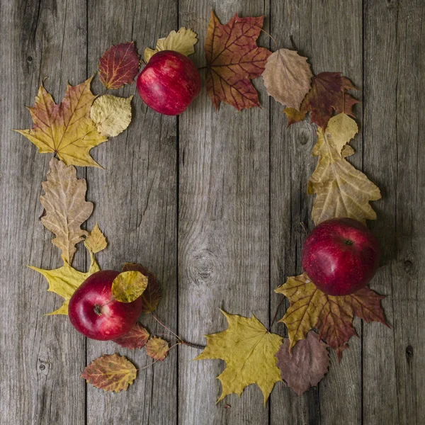 Komposisi musim gugur. Kemarahan yang terbuat dari daun musim gugur dan apel merah pada latar belakang kayu tua. Tiang datar, tampilan atas, ruang fotokopi. Mockup , Stok Foto