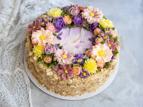 Bolo de Napoleão com nata de baunilha, decorado com flores de creme de manteiga - rosas, escabioses, crisântemos em cores rosa, amarelas, roxas. Estilo vintage. Fundo cinzento, guardanapo de renda. Espaço de cópia — Fotografia de Stock