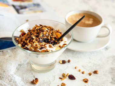 Sağlıklı kahvaltı. Granola, balkabağı tohumlu müsli, bal, cam kasede yoğurt beyaz arka planda bir fincan kahve. Modern bir kızın kahvaltısı. Kapat, boşluğu kopyala.
