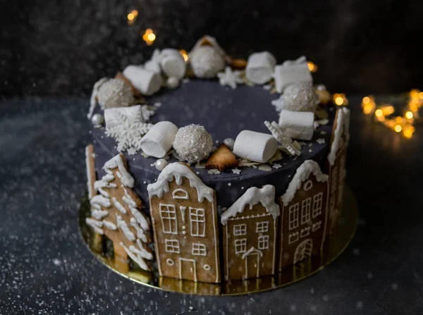 Kue abu-abu Natal yang dihias dengan kue jahe dalam bentuk rumah dan pohon bersalju, marshmallow, kepingan salju, permen. Natal, kartu ucapan Tahun Baru. Latar belakang abu-abu dengan karangan bunga. Salin ruang . Stok Lukisan  