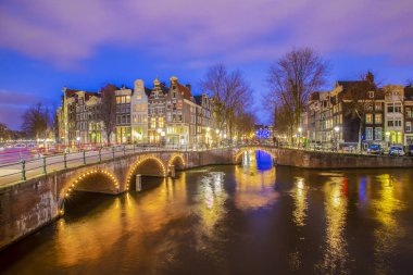 Amsterdam 'daki romantik kanal Leidsegracht' a gece şehir ışıkları, köprüler ve su üzerindeki yansıma