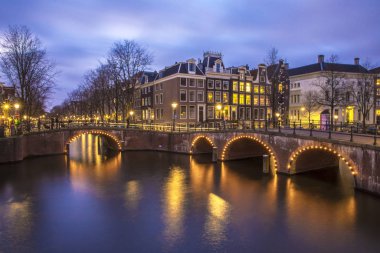Amsterdam 'daki romantik kanal Leidsegracht' a gece şehir ışıkları, köprüler ve su üzerindeki yansıma