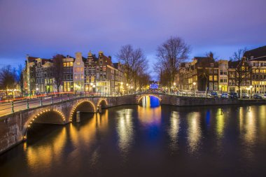 Amsterdam 'daki romantik kanal Leidsegracht' a gece şehir ışıkları, köprüler ve su üzerindeki yansıma